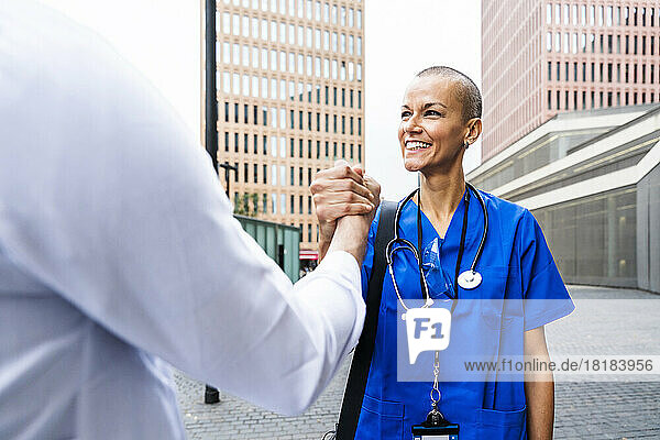 Smiling mature nurse holding hand of doctor on footpath