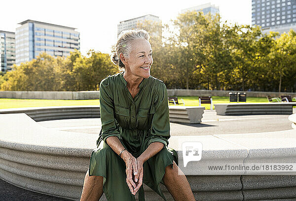 Lächelnde reife Frau sitzt auf einer Bank im Park