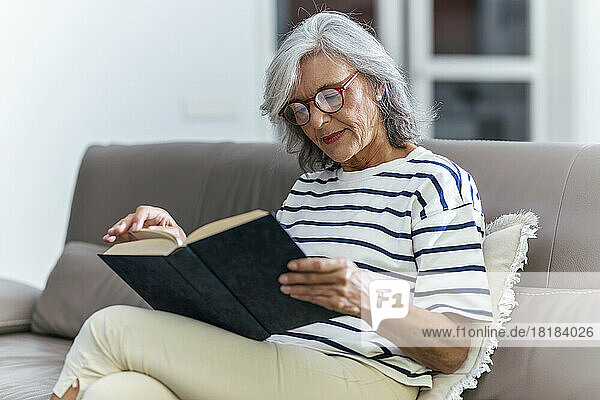 Senior woman wearing eyeglasses reading book at home