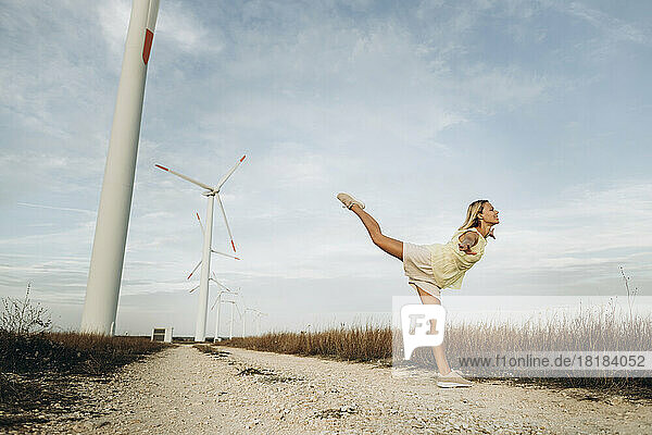 Woman standing with arms outstretched by wind turbines on field