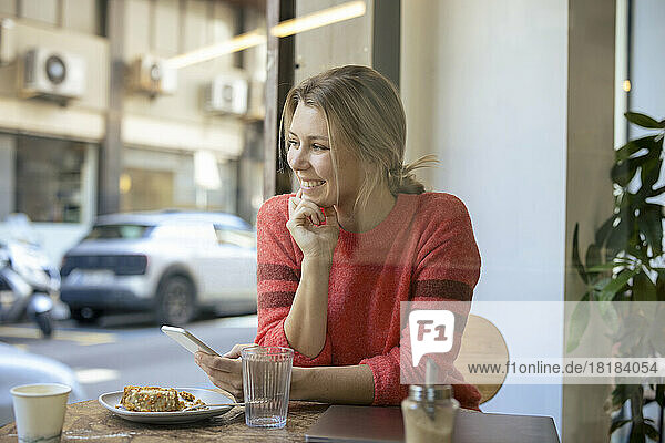 Happy freelancer sitting with food using smart phone in cafe