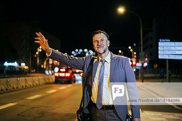 Smiling mature businessman hailing cab on street