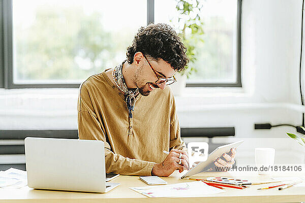 Happy illustrator wearing eyeglasses using digital tablet at desk