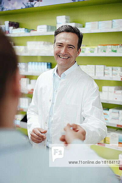 Happy pharmacist giving medicine to customer at store