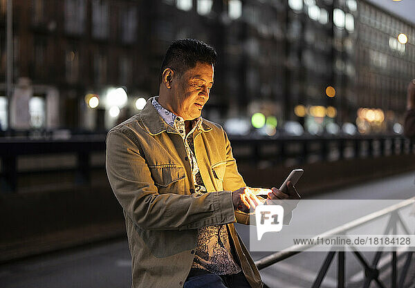 Mature man using smart phone sitting on railing