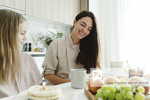 Smiling woman with daughter at dining table in kitchen