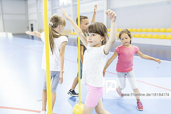 Elementary students with arms raised running around pole at school sports court