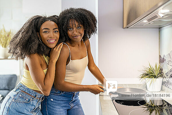 Young friends with cooking pan on glass stove in kitchen