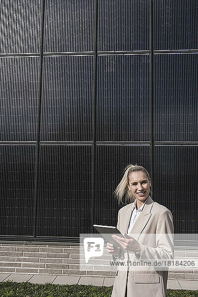 Happy businesswoman standing with tablet PC in front of solar panels