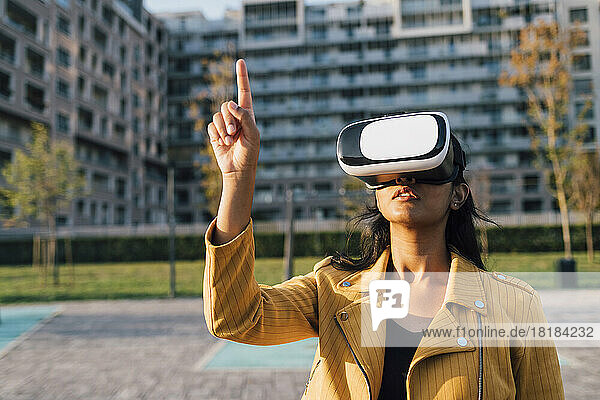 Young woman gesturing with virtual reality simulator in front of building