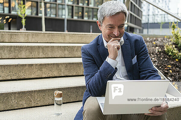 Mature businessman looking at laptop sitting on steps