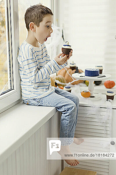 Surprised boy sitting with cupcake on window sill