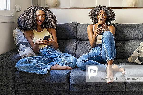 Young friends using smart phones sitting on sofa in living room