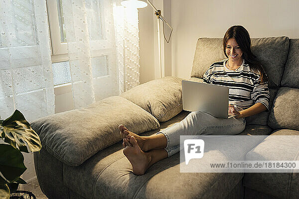 Happy woman using laptop on sofa at home