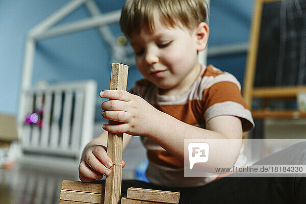 Smiling boy playing with wooden block in bedroom at home