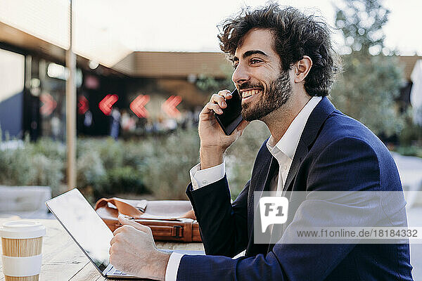 Happy businessman talking on smart phone sitting in cafe