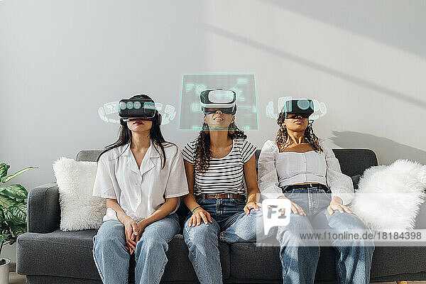 Friends wearing virtual reality glasses sitting on sofa at home
