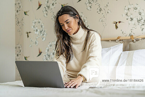 Smiling young freelancer using laptop on bed at home