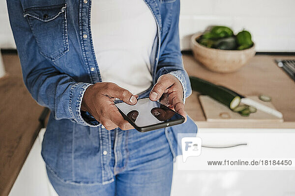 Hände einer Frau  die zu Hause ihr Smartphone an der Küchentheke benutzt