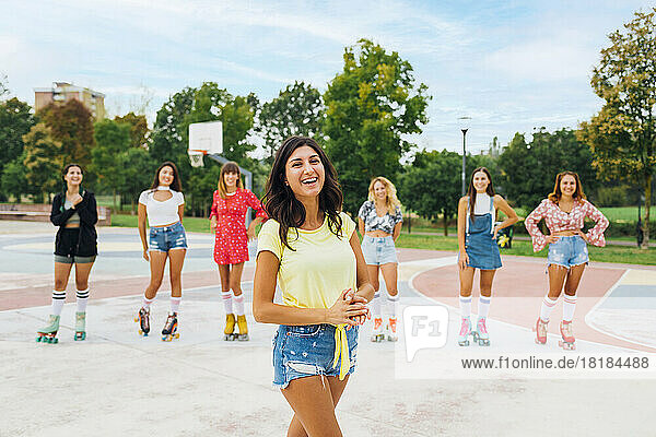 Happy woman standing in front of friends wearing roller skates at sports court