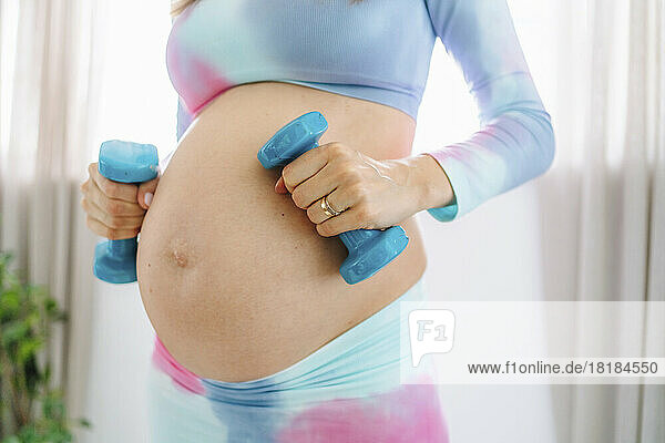 Pregnant woman holding dumbbells at home