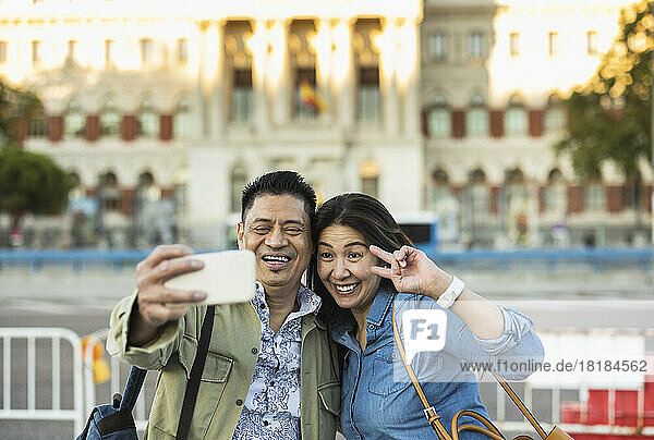 Smiling man with woman taking selfie through mobile phone on footpath