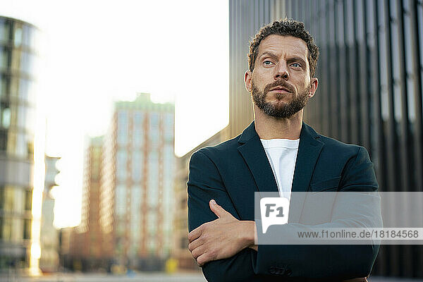 Businessman standing with arms crossed contemplating in city