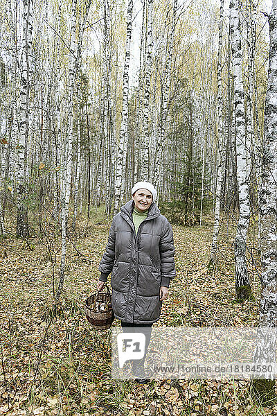 Smiling senior woman holding basket of mushrooms in forest