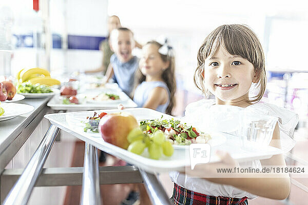 Smiling girl with food and fruits on tray at lunch break in cafeteria