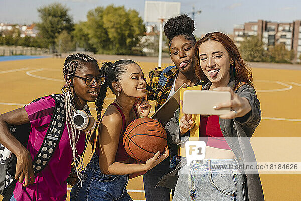 Happy young woman with friends taking selfie through smart phone at sports court