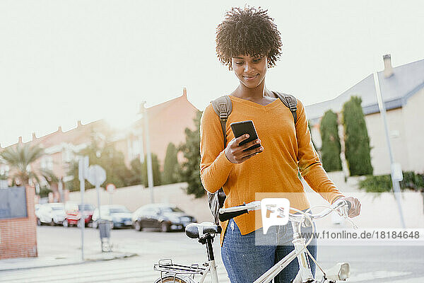 Woman with bicycle using mobile phone on street