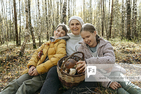 Smiling grandmother  boy and girl sitting with basket of mushrooms in forest