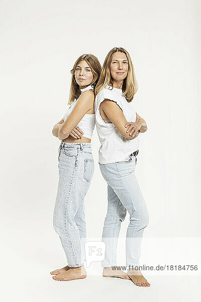 Confident mother and daughter standing with arms crossed in studio
