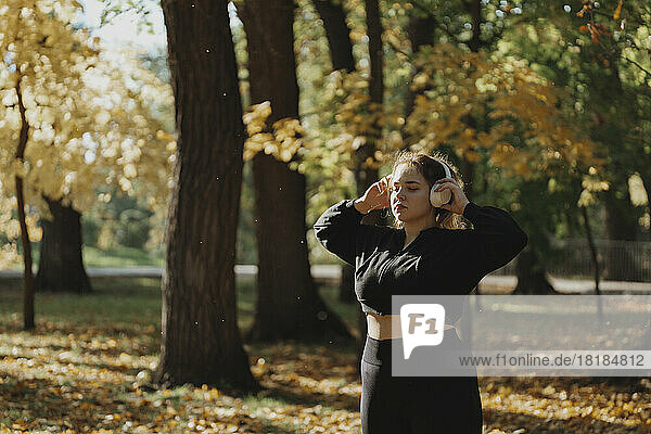 Young woman with eyes closed enjoying music listening through wireless headphones in park