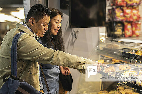 Mature couple shopping pointing at food on display in bakery