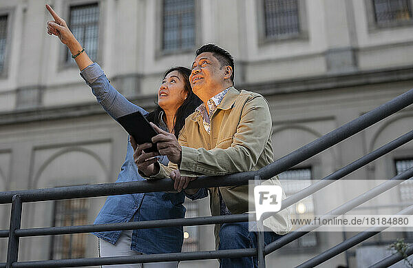 Woman gesturing by man holding tablet PC leaning on railing