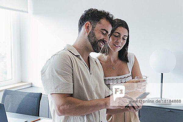 Smiling businessman sharing smart phone with businesswoman in office