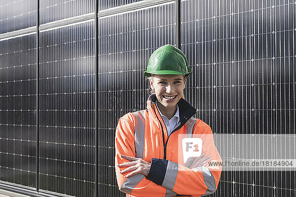 Happy female engineer with arms crossed standing in front of solar panels