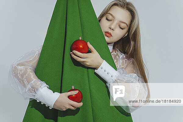 Girl holding red baubles embracing abstract Christmas tree against white background