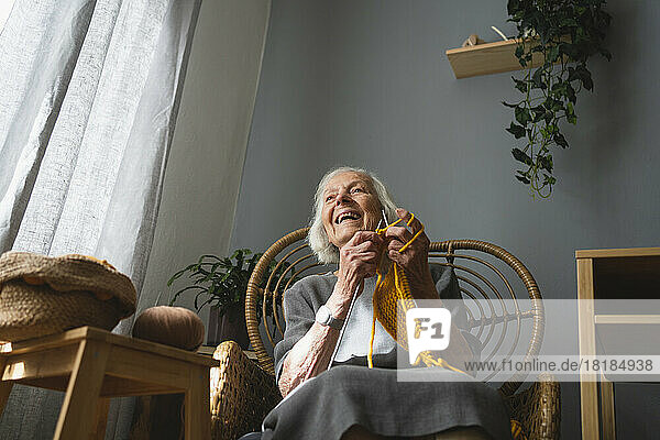 Happy senior woman knitting on chair in living room