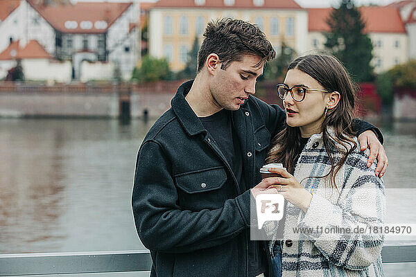 Young couple holding disposable coffee cup in front of river