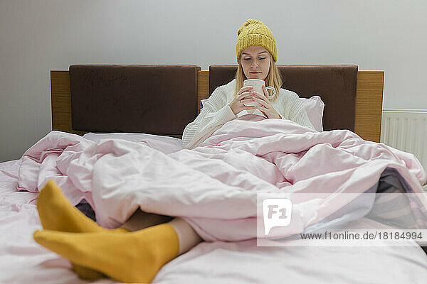 Young woman with coffee cup sitting on bed at home