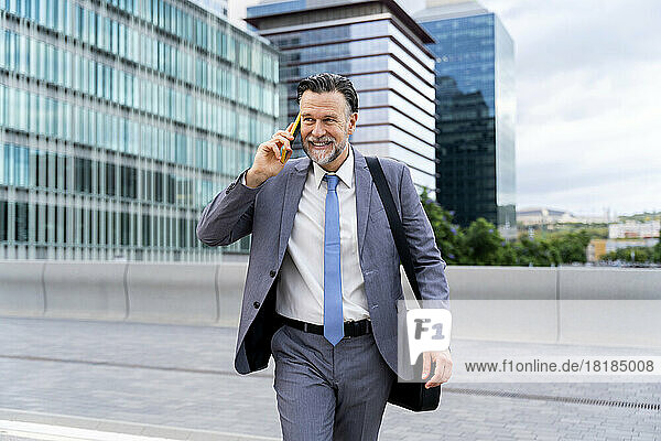 Lächelnder reifer Geschäftsmann  der mit seinem Smartphone auf der Straße spricht