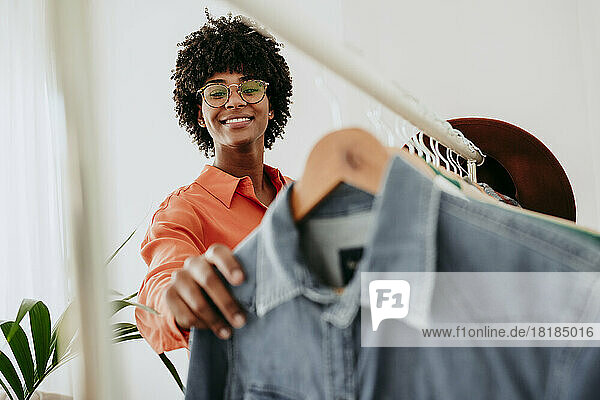 Smiling businesswoman wearing eyeglasses holding clothes at home office