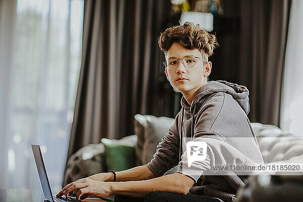 Teenage boy with laptop sitting on sofa at home