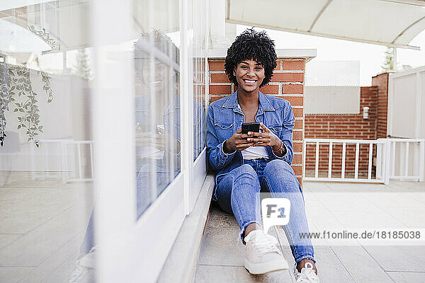 Happy young woman with smart phone sitting on porch