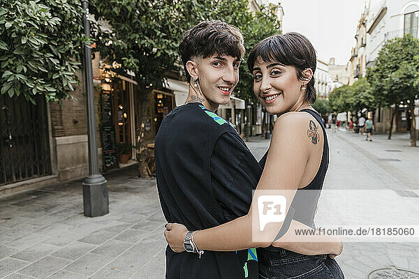 Lächelndes junges Paar  das sich auf dem Fußweg umarmt