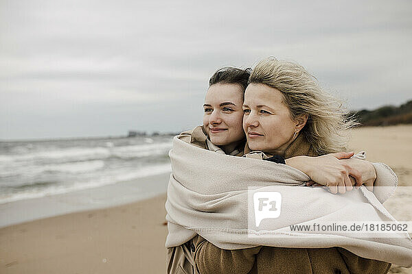 Mother and daughter wrapped in blanket at beach