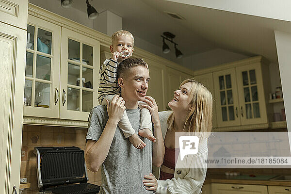 Happy woman with man carrying son on shoulders in kitchen at home