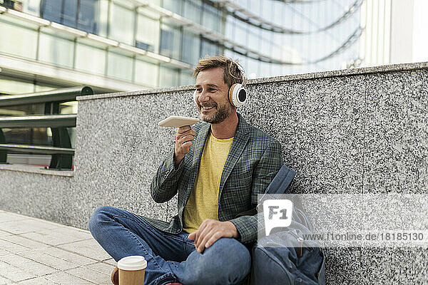 Happy man talking on speaker phone sitting by wall